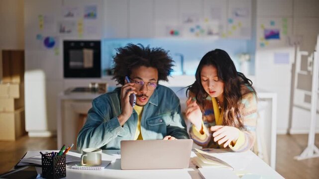 Diverse team discussing project home office. Man phone call woman points laptop.