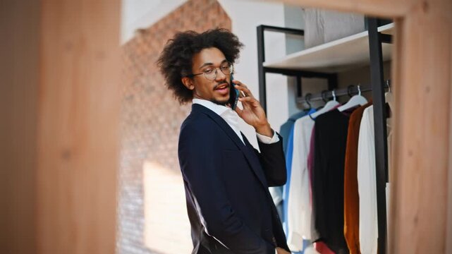 Business man talking phone clothing store. Smiling customer near suit wardrobe.
