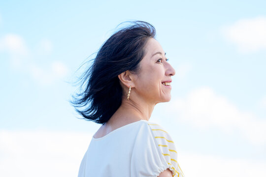 笑顔で髪を風になびかせるシニア女性　空バック