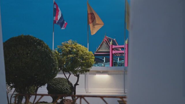 National flag of thailand and a dharmachakra flag waving in the wind with a traditional temple