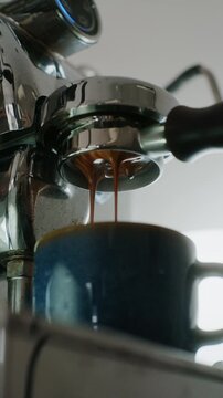 4K vertical Pouring coffee stream from professional machine in cup. Barista man making double espresso, using filter holder. Flowing fresh ground coffee. Drinking roasted black coffee in the morning