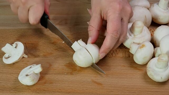 Raw mushrooms champignons are cut into slices with a knife on a wooden cutting Board. Close up.