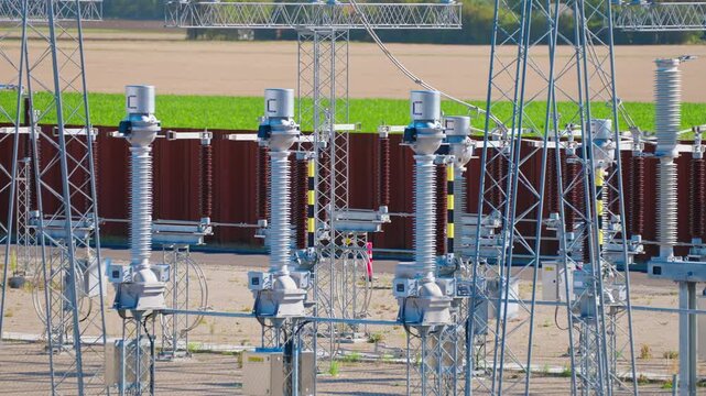 Slow push-in on high-voltage switchgear and insulators inside an outdoor electrical substation, showing equipment used for switching, isolation and control of transmission circuits.