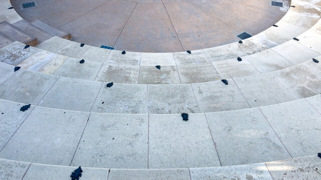 curved concrete amphitheater steps descend toward a round stage featuring small dark leaf shaped deterrents on each tier