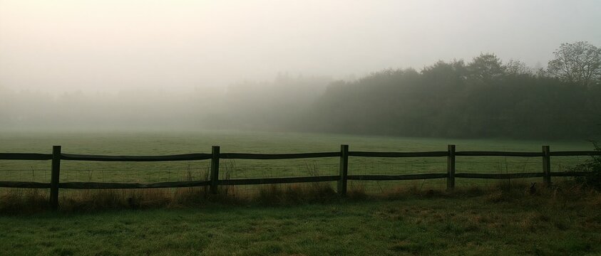 Autumn fog over a misty grey field with a damp timber fence, creating a muted atmospheric background for compositing and copy space