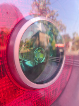 Close-up view of a car's rear brake light, showing an LED bulb with soft reflections of trees and a road.