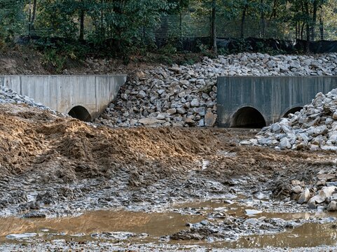 Drainage pipes set into concrete headwalls at a construction site with muddy soil and waterlogged ditches for civil engineering and flood control