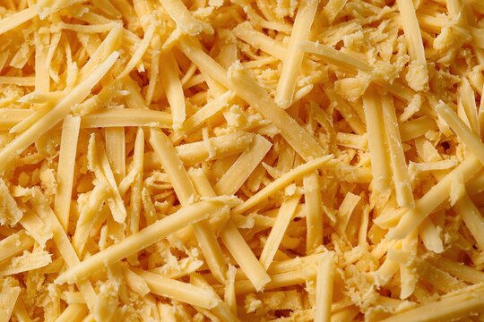 Shredded cheese food texture with buttery yellow grated dairy strands, creating a dense tactile surface for culinary backgrounds and packaging