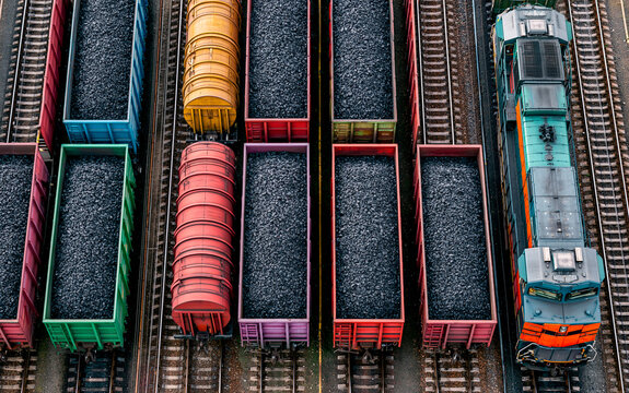 Colorful freight train cars filled with coal parallel railway tracks, industrial transportation scene with vibrant wagon, overhead view, energy supply and resource, organized railway yard