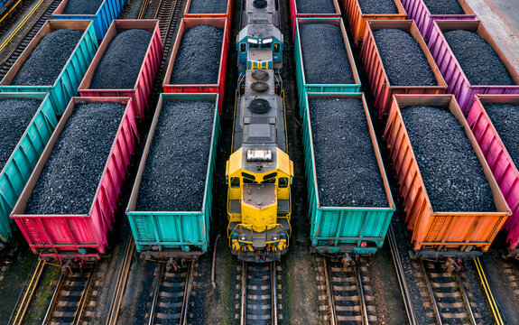 Colorful freight train cars filled with coal parallel railway tracks, industrial transportation scene with vibrant wagon, overhead view, energy supply and resource, organized railway yard