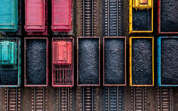 Colorful freight train cars filled with coal parallel railway tracks, industrial transportation scene with vibrant wagon, overhead view, energy supply and resource, organized railway yard