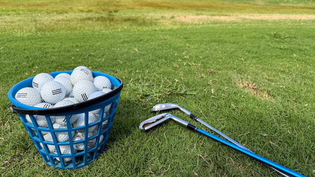 Basket of used golf balls with golf clubs on green grass at a driving range, golf practice and training equipment outdoors.