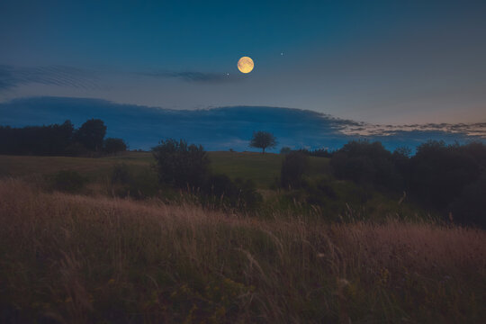 Full Moon, stars and planets above landscape silhouettes in blue hour time.