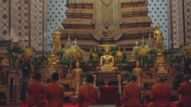 Buddhist monks praying and meditating in front of a giant golden buddha statue inside wat arun temple