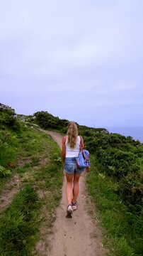woman walking along scenic coastal trail outdoors in nature with backpack- vertical video