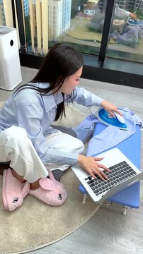Asian Woman Multitasking With Laptop and Ironing Clothes at Home