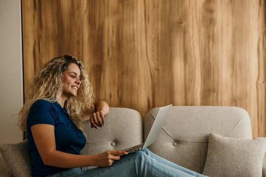 Young woman smiling working remotely using laptop on sofa