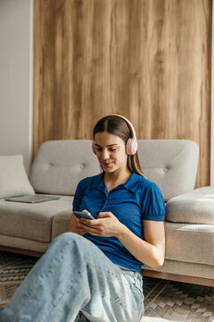 Young woman relaxing at home using smartphone and headphones