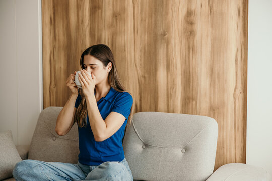Woman relaxing on sofa drinking warm beverage at home