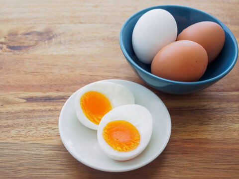 Soft boiled egg cut in half on a white plate and white and brown eggs in a blue bowl on a wooden table, top view with copy space