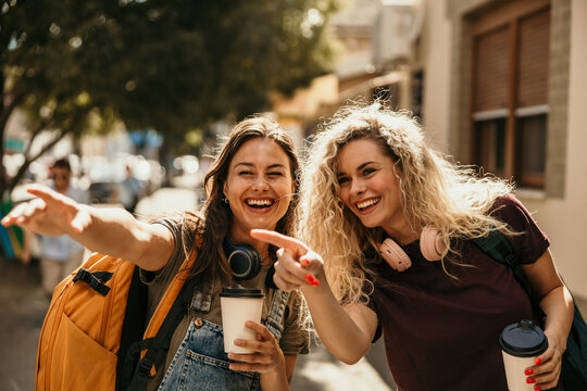 Two young women friends traveling laughing pointing street