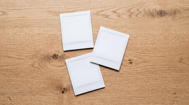 Top view of three blank white instant photo frames scattered on a natural wooden table surface, flat lay mockup template with copy space.