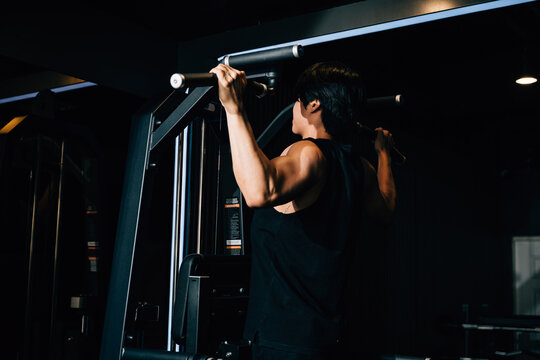 Back view of Asian man pulling up showing back muscle at gym, men doing pullups bar machine in fitness gym, workout healthy lifestyle