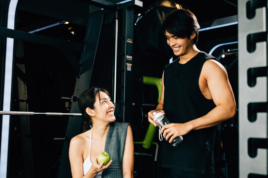 Young couple talking together after workout at gym, man hold water sport from bottle and woman holding green apple in fitness gym, eating healthy food after exercise, workout healthy lifestyle