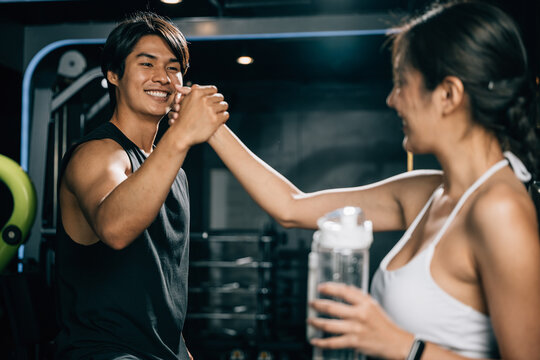 Asian woman and man working out together in gym interior and holding hands, smile couple holding hold hand after complete training at fitness gym, sport workout healthy lifestyle