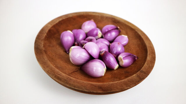 Fresh peeled red shallots served on traditional round wooden plate