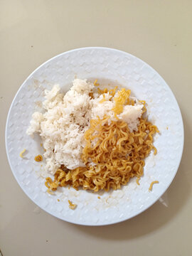 Fried instant noodles served together with steamed white rice on round plate