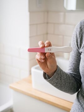 Hand holding a positive pregnancy test at home. Home pregnancy testing and fertility planning. Family planning, conception and reproductive health. Parenthood and expecting a baby.