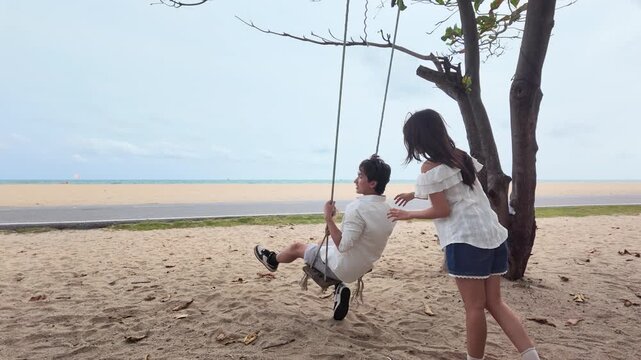 Young Couple Having Fun on a Wooden Tree Swing by the Beach