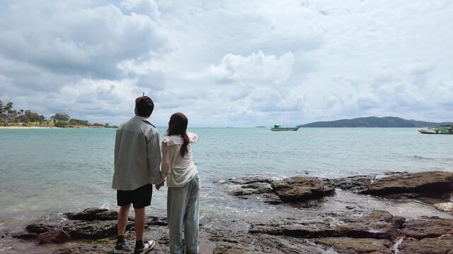 Young Couple Holding Hands and Looking at Sea on Rocky Shore