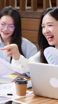 Asian Businesswomen Laughing and Discussing Documents in Modern Office