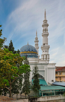 Al-Bukhari Foundation Mosque featuring a decorative blue patterned dome and tall white minarets, framed by green foliage under a cloudy blue sky in Kuala Lumpur, Malaysia