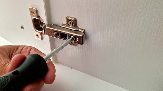 Adjusting a cabinet door hinge with a screwdriver to improve alignment and ensure smooth, proper door operation during furniture installation or home repair