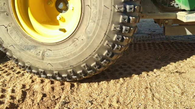 Close view of tractor tire and metal rake attachment smoothing sand in bunker hazard on golf course