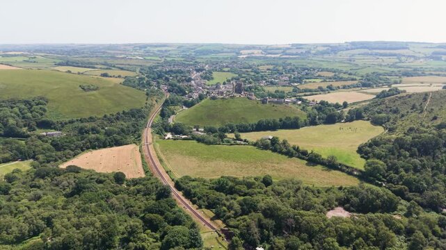 Corfe Castle Isle of Purbeck Doirset, England, high forward drone footage along Swanage to Corfe railway towards the famous castle with views of the surrounding countryside on bright sunny day