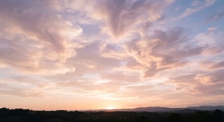 Obraz premium Soft pink and peach clouds spreading across the sky at sunset