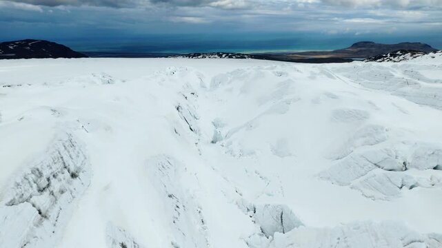 Kviarjokull glacier spreads across a broad snow covered ice surface with coastal mountains and the Atlantic Ocean visible beyond, captured during a drone forward flyover.