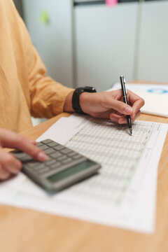 Person checks financial figures with a pen and calculator on a printed report, focusing on accounting analysis, budgeting and accurate calculation.