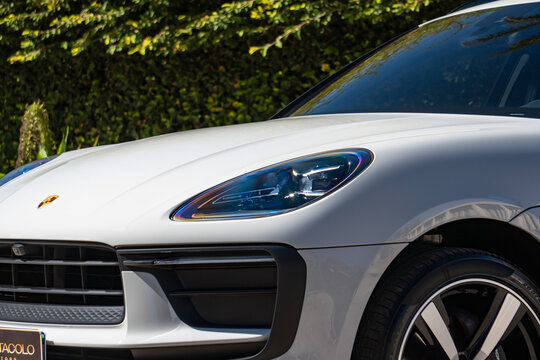 White Porsche Macan Luxury SUV Front Headlight Detail Close Up Outdoor Green Hedge Background
