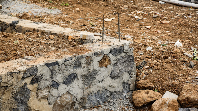Stone and concrete building foundation with exposed steel rebar on raw soil at an active construction site.
