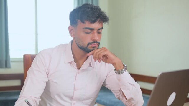 Young male professional listening attentively and taking notes during an online business meeting while working from home. Focused workplace scene suitable for virtual meetings an remote work concepts.