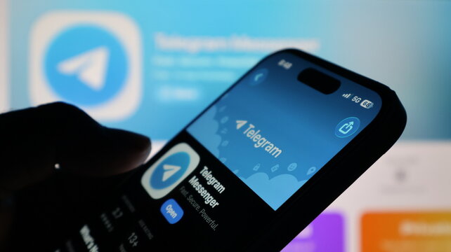 Telegram app store page open on modern smartphone screen in front of computer monitor.