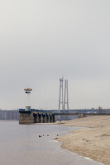 Fototapeta premium Gloomy riverfront with an old pier and a bridge under construction