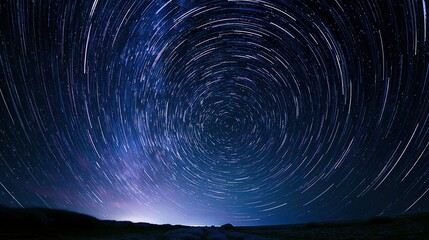 Fototapeta premium Mesmerizing star trails in a swirling vortex over a dark, silhouetted landscape at night