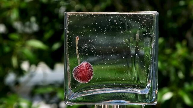 Fresh red cherry submerged in sparkling water inside a glass container
