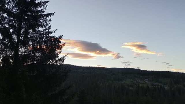 Golden sunset clouds glowing above silhouetted pine forest hills in the Carpathian mountains, peaceful evening sky